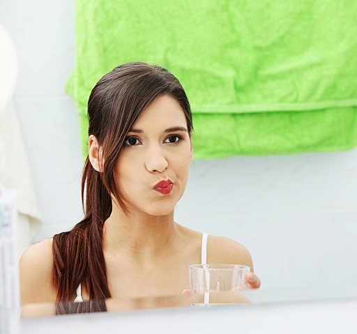 Young beautiful brunette woman using mouthwash at her bathroom